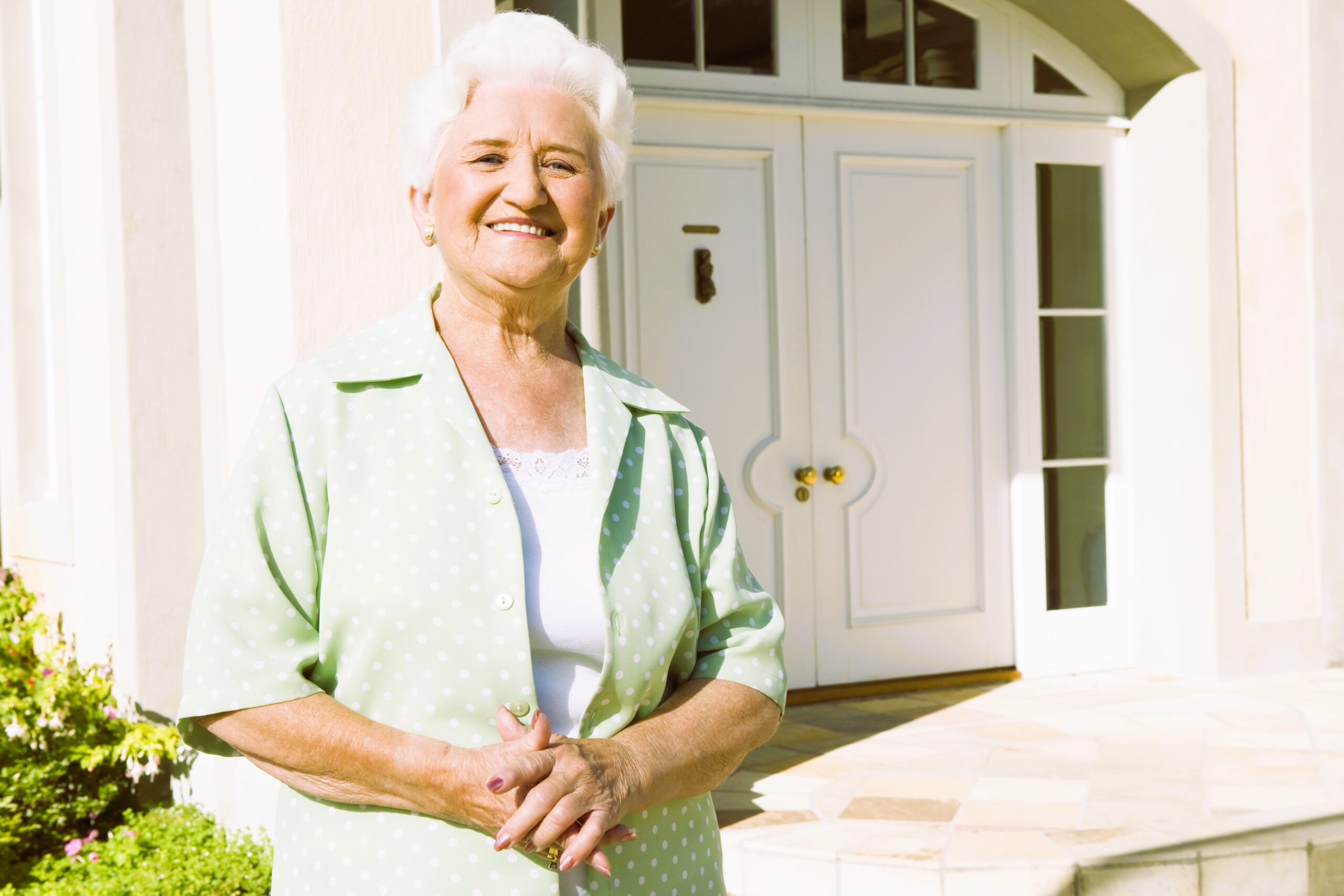 Senior woman standing outside front door of house