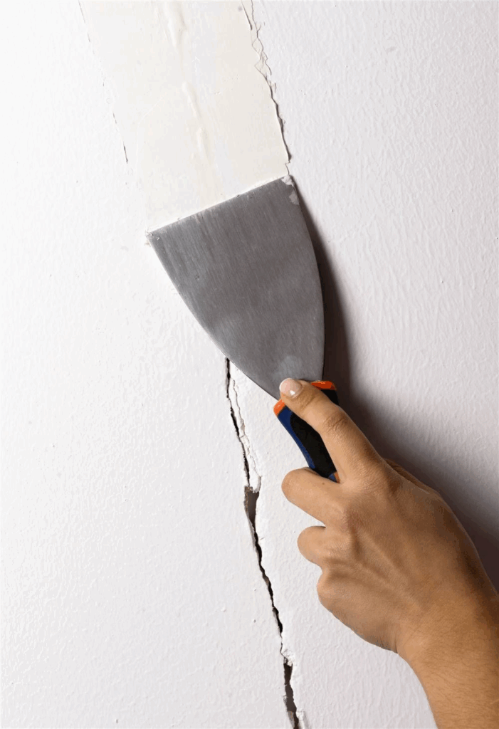 Repairing wall crack with putty knife and filler