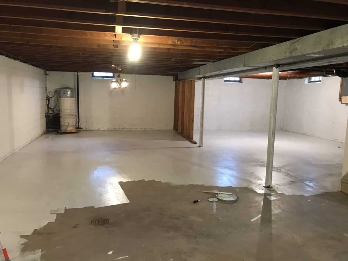 Unfinished basement floor being painted with waterproof sealant coating